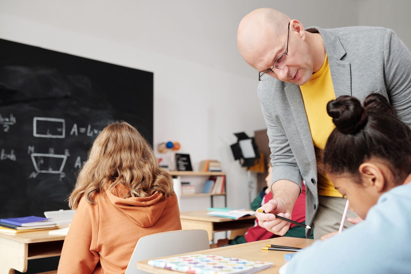 A teacher leaning over a desk to help two students with their work